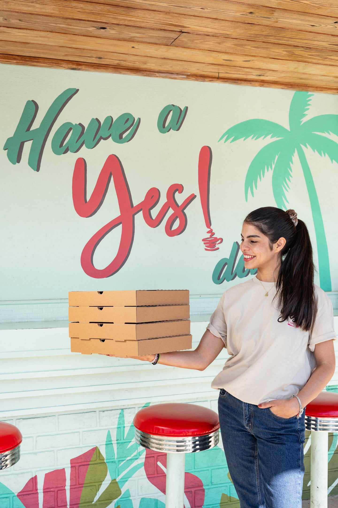 A team member holding a stack of pizza boxes in front of the Have a Yes! day mural