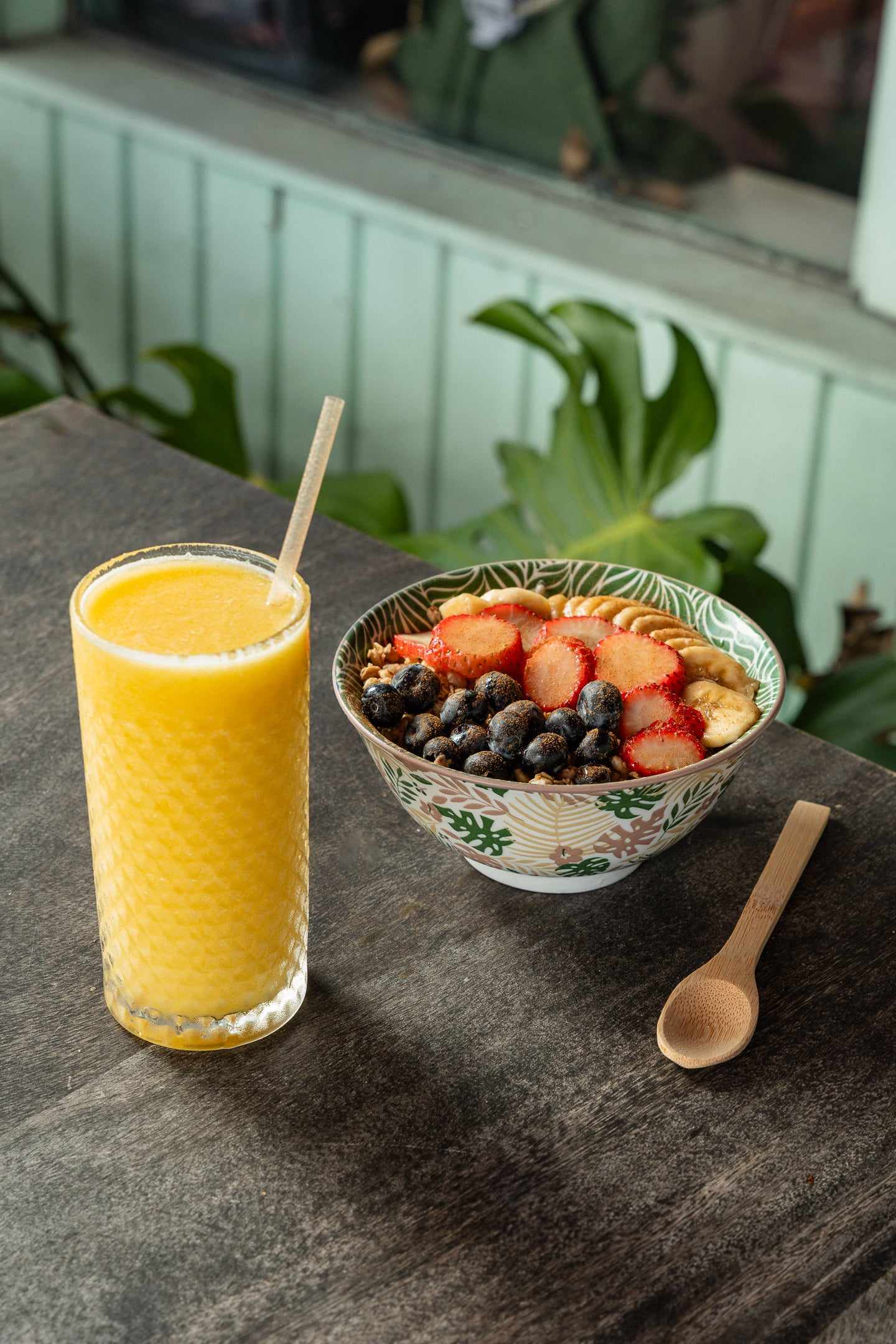 A glass of fresh orange juice next to a bowl of yogurt with strawberries, banana and blueberries